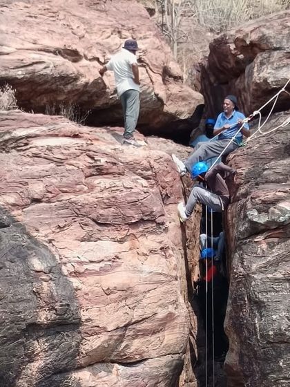 A team works together to manage the ropes for a climber in a narrow rock chimney at Badami, demonstrating advanced techniques.