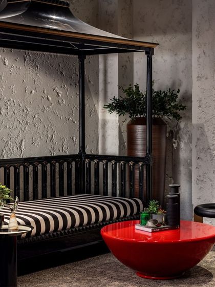 This seating nook in the basement of the House of Two Worlds features a custom canopy bed, textured walls, and a bold red coffee table. The material choices create a distinct and immersive character, setting it apart from the home's primary living spaces.