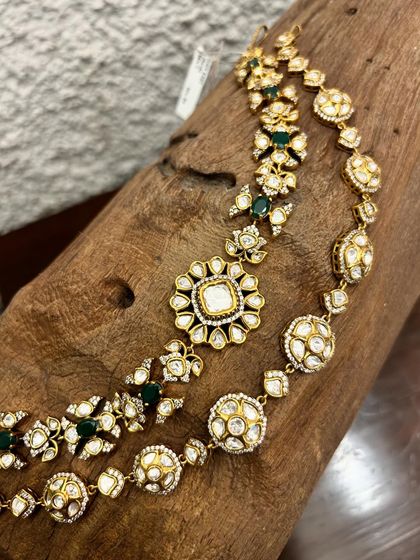 A close-up of two beautiful kundan necklaces, one with green stones and a floral motif, and the other a classic design with round pendants.