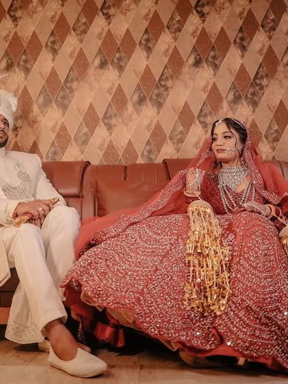 A regal portrait of the bride and groom seated on a leather sofa, showcasing their traditional wedding attire.