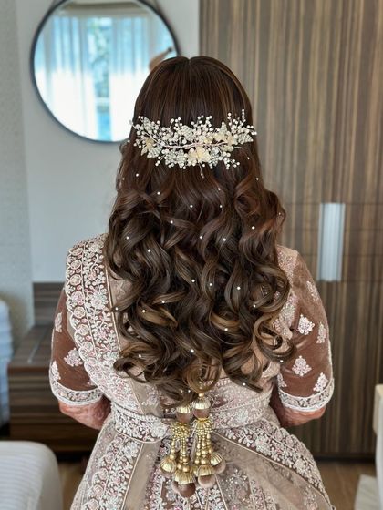 A dreamy half-up style with voluminous curls, adorned with a sparkling hairpiece and scattered pearls. This is a perfect look for a fairytale reception.