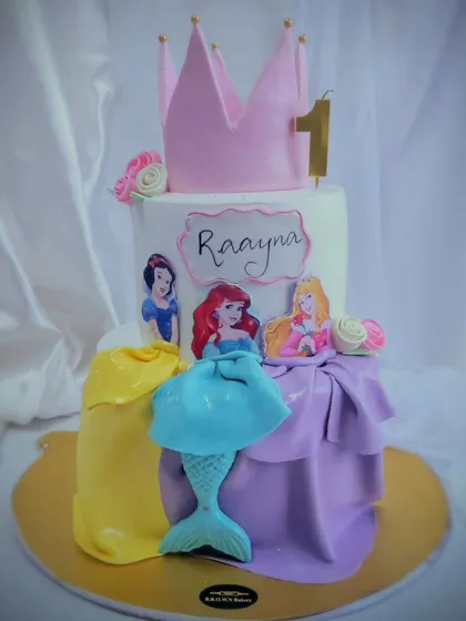 A Disney Princess dream cake for a first birthday. This two-tier design features Snow White, Ariel, and Rapunzel, with their iconic dresses recreated in fondant, all topped with a princess crown.