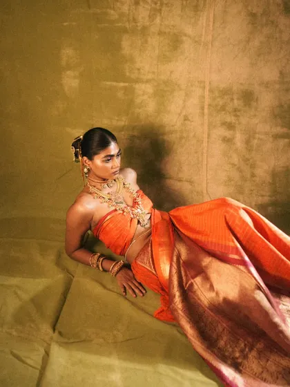 A full-length shot showing the beautiful drape of the sari and the complete makeup and hair look for 'Swaṟṇavalli'. The pose and lighting create a painterly, classic feel.
