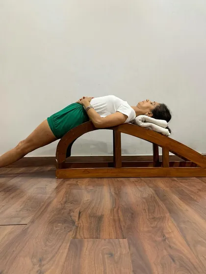 The backbend bench is a specialized prop designed for deep, supported backbends. In this Purvottanasana variation, it provides a firm, contoured surface to open the entire front of the body safely and effectively.