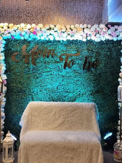 A classy 'Mom To Be' baby shower setup. We used a green foliage wall as the backdrop, framed with pastel flowers and accented with elegant lanterns on stands.