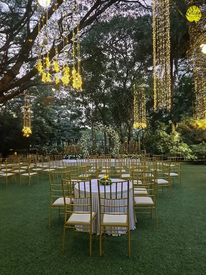 An evening view of our lawn set up for a wedding, with tables arranged for guests under a canopy of trees adorned with beautiful, glowing lanterns.