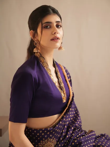 A close-up of Sanjana Sanghi, highlighting the intricate details of the gold-plated necklace and earrings that frame her face.