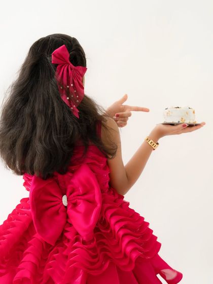 A cute shot from behind, showing off the large bow on her dress as she points towards her birthday cake.