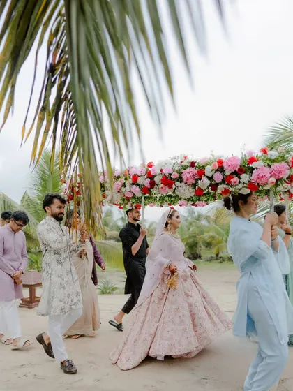 The bride's grand entry under a lush floral canopy, carried by her brothers, on the sandy shores of Goa.