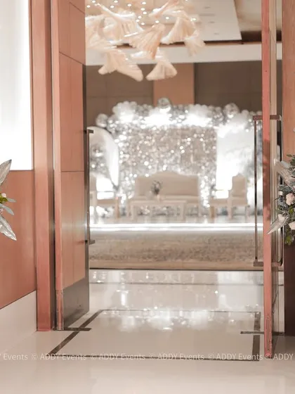 A chic and modern entrance to a grand celebration. The doorway is flanked by metallic floral stands, offering a glimpse of the glamorous decor inside.