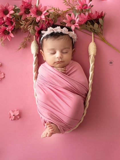 Pretty in pink. A sleeping newborn is swaddled in a pink wrap and rests on a floral swing.