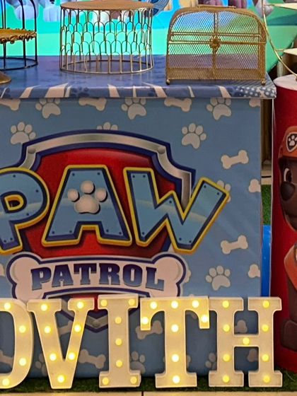 A detailed shot of a Paw Patrol themed dessert table. The table is wrapped in a custom print, and it's accompanied by a character cutout and light-up marquee letters.