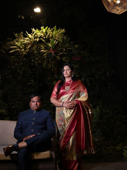 The parents of the groom posing for a formal portrait. The mother's ornate saree is perfectly balanced by the father's classic navy bandhgala, creating a portrait of sophistication.
