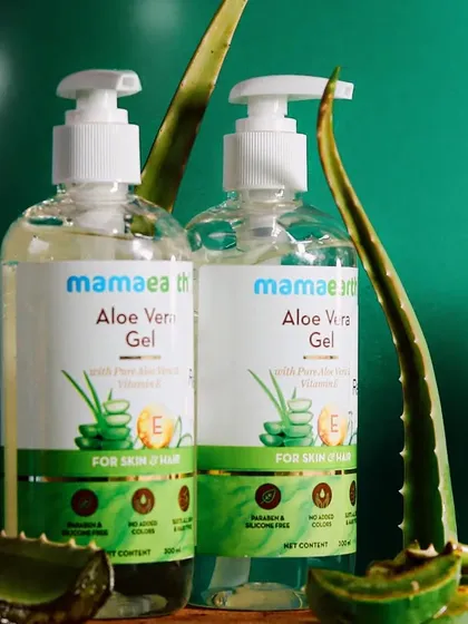 A tighter crop on the Mamaearth Aloe Vera Gel bottles, focusing on the labels and the fresh aloe leaves to reinforce the product's natural formulation.