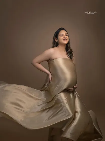 A joyful shot from a maternity photoshoot. The soft, natural makeup ensures the focus remains on her happy expression and the beautiful movement of the fabric.