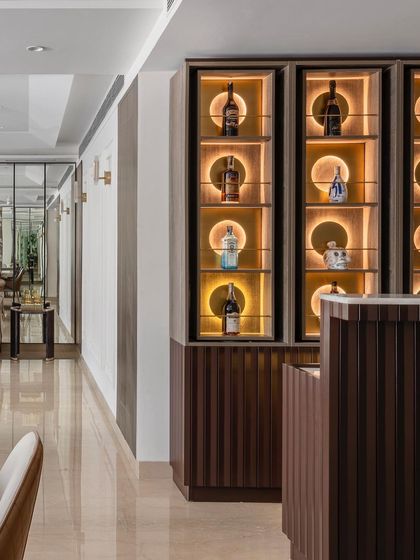 The bar area is a study in refined detail, featuring a fluted wooden counter and a stunning back-lit display with rotating shelves. This space is designed to be both a functional serving area and a decorative highlight.