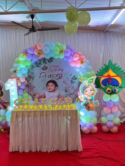 A premium decor combining a first birthday and naming ceremony. This princess and Radha Krishna theme uses pastel balloons, character cutouts, and a custom ring backdrop.