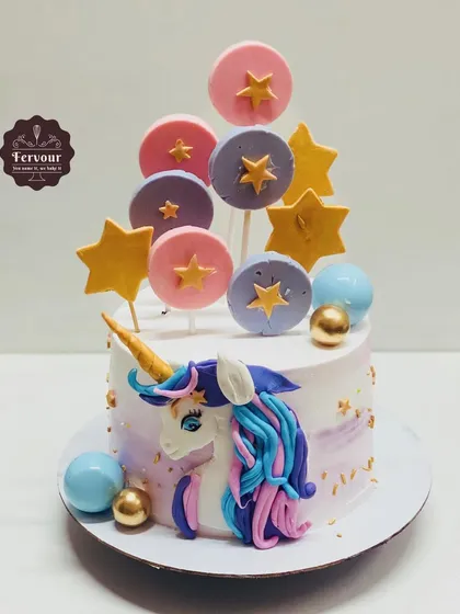 A unicorn cake decorated with colourful lollipops and stars. This chocolate almond cake uses minimal fondant, with the unicorn's head and decorations crafted to sit on a whipped cream base.