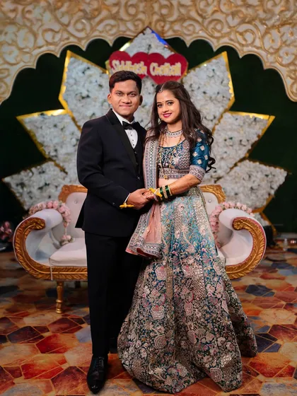 A formal portrait of the couple on their wedding reception stage, posing against a beautifully decorated floral backdrop.