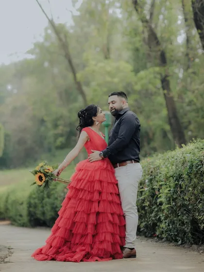 A beautiful pose during a pre-wedding session in a Pune garden. The woman's vibrant red dress stands out against the green foliage, creating a visually stunning and romantic photograph.
