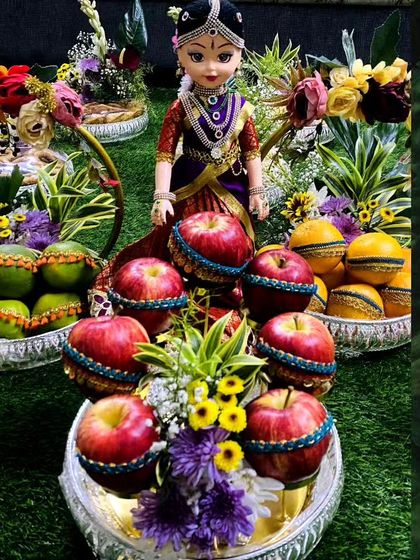 This doll, dressed in a purple silk pavadai, is the centerpiece of a fruit platter arrangement. I use decorated apples and oranges to create a colorful and auspicious display for any celebration.