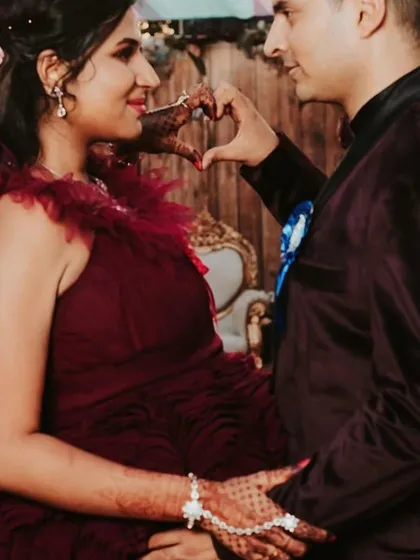 A sweet moment making a heart shape over the baby bump. This close-up shows the delicate texture of our ruffled maroon gown.