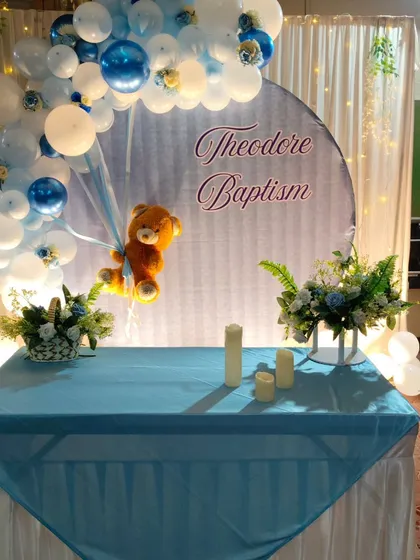 The decorated cake table for 'Theodore's Baptism'. The table is set up in front of the main backdrop and features matching floral arrangements.