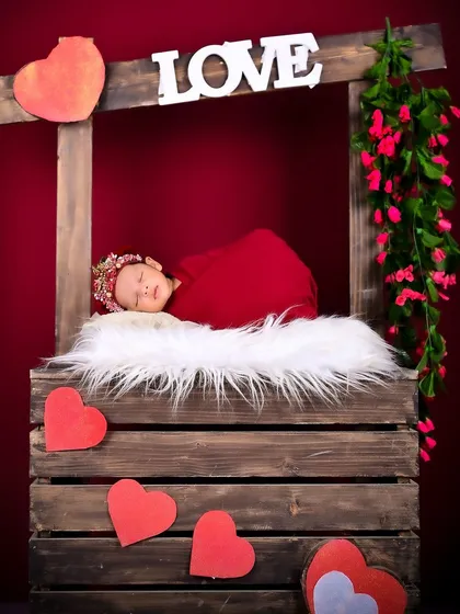 A newborn peacefully sleeping in a love-themed setup. The rich red background and soft fur create a warm and romantic feel for this portrait.