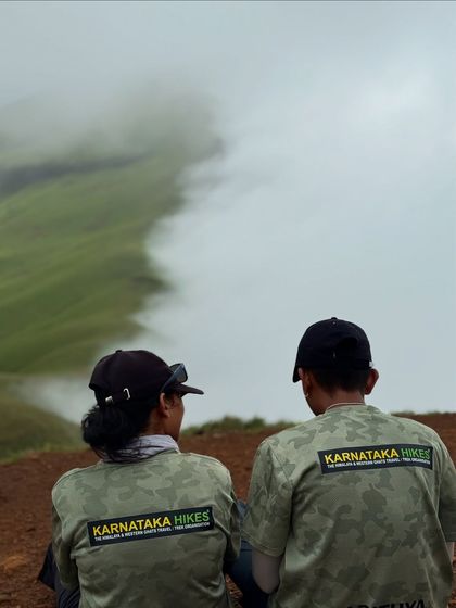 Two of our team members in Karnataka Hikes gear, looking out at the clouds rolling over the Netravathi ridge.