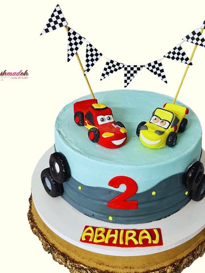 The full view of this 'Cars' themed cake for Abhiraj's second birthday. The handmade car toppers, checkered flags, and road design create a perfect racetrack for a little fan.