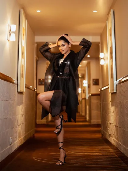 A dynamic, full-length pose in a hotel corridor. The one-legged stance and strong posture showcase the avant-garde design of the Amit Aggarwal outfit, creating a powerful editorial image.