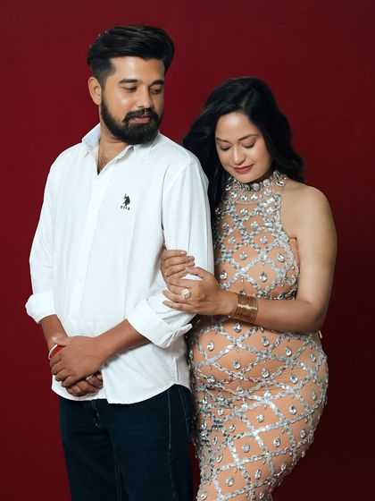 A lovely couple's portrait from a glamorous studio session. The partner stands close to the mother-to-be, who shines in her sparkling gown, creating a picture of elegance and togetherness.
