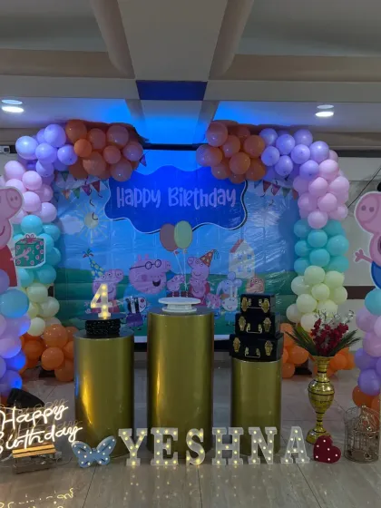 A colorful Peppa Pig themed 4th birthday party. The setup features cutouts of Peppa and George, a vibrant balloon arch, and a 'Happy Birthday' neon sign.