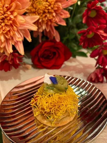 A modern twist on Sev Puri, with a mountain of crispy sev and a dollop of chutney, garnished with an edible flower.