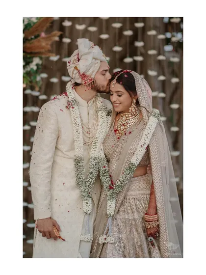 A classic wedding portrait of a couple in beautiful pastel outfits. The groom's affectionate kiss on her forehead and their gentle smiles capture the happiness of their union.