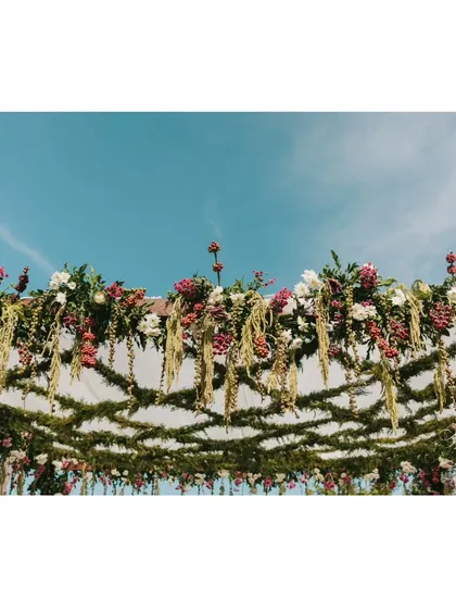 A low-angle shot looking up at the mandap ceiling, showing the intricate web of jasmine and the hanging coffee berry strands against the sky.