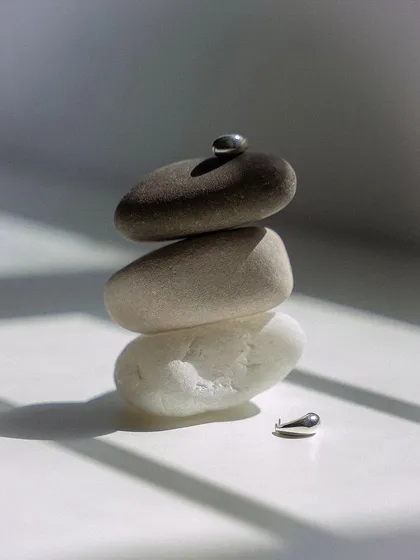 A minimalist still life composition for a jewelry shoot. The smooth, stacked stones and the play of natural light and shadow create a serene and balanced setting for the delicate silver earrings.