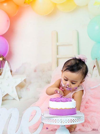 Focused on the task at hand. This shot shows her digging into the cake, surrounded by a dreamy setup of clouds and pastel balloons.
