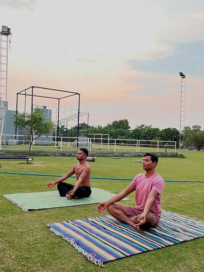 Finding peace and inner stillness. Two members sit in a cross-legged meditation pose, connecting with their breath and the serene outdoor environment at sunset.