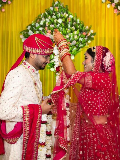 The groom places the varmala on the bride, a moment of mutual respect and love, set against a vibrant yellow backdrop.