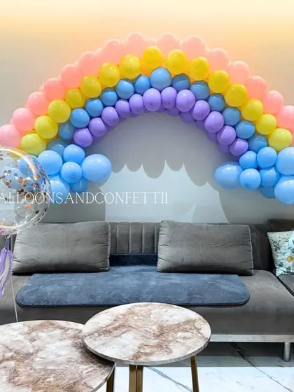 A simple yet beautiful pastel rainbow balloon arch over the sofa, perfect for a happy and colorful home celebration.