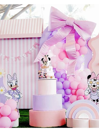 A grand Minnie and Daisy themed setup, featuring a large pink bow, character cutouts, and a multi-tiered cake, all in a lovely pastel color scheme.