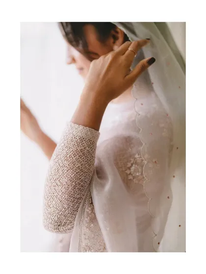 A close-up of the bride's hands as she adjusts her delicate, scalloped veil. This shot highlights the fine details of her attire and the grace in her movements.