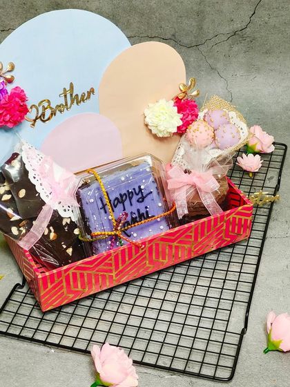 A closer look at our curated Rakhi hamper. This gift includes a personalized bento cake, chocolate bark, and a mini bouquet of cake pops, all beautifully arranged in a decorative box with "Brother" and "Sister" tags.