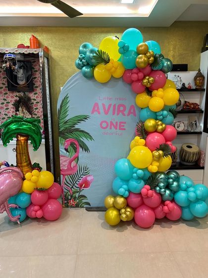 A vibrant tropical flamingo theme for a first birthday at home. This setup includes a personalized backdrop, a colorful balloon garland, and a flamingo prop.