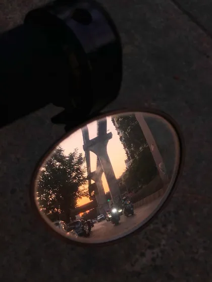 A creative shot capturing the reflection of a Mumbai sunset and street scene in a motorcycle's side-view mirror.