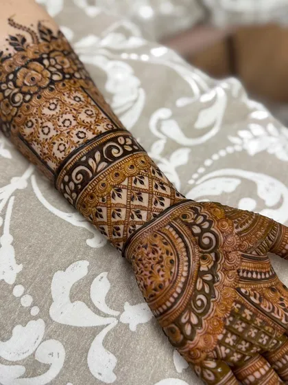 A close-up view of a highly detailed Indian henna design. This piece features a wide cuff with geometric lattice work, intricate floral bands, and delicate patterns covering the palm and fingers.