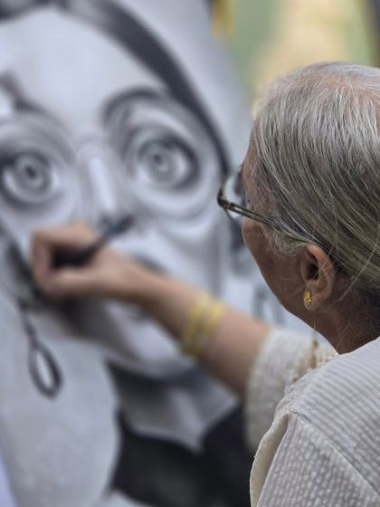 A tight shot focusing on the student's hand as she carefully shades the face in her charcoal portrait.