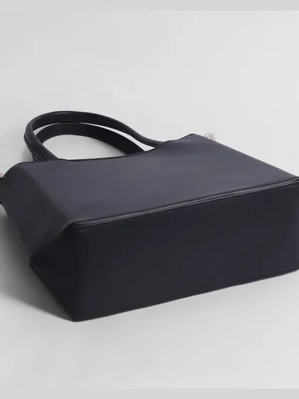 The base of a black handbag, photographed to show its shape and structure.