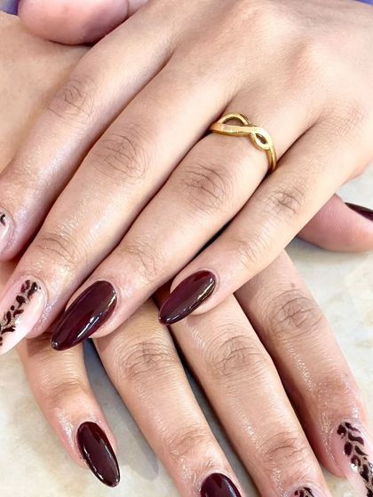 Another view of this elegant burgundy and nude manicure, showcasing the delicate, hand-painted leaf details and the glossy finish.
